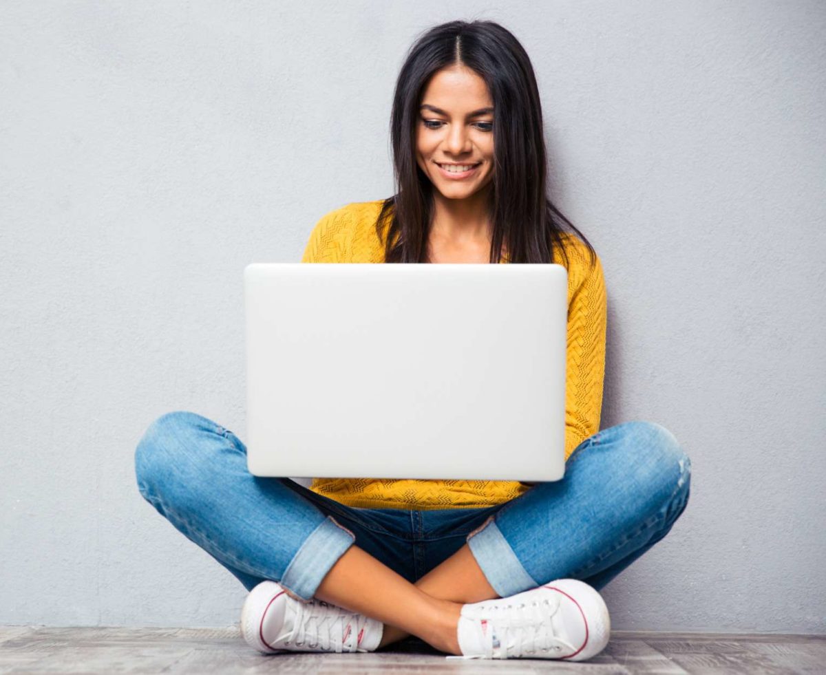 Une femme assise en tailleur contre un mur avec un ordinateur portable
