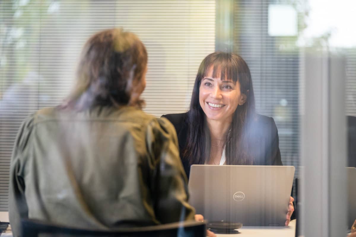 Deux femmes discutent dans un bureau vitré